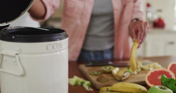 Hands of biracial woman composting vegetable waste in kitchen