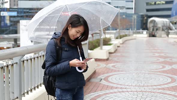 Woman texting message on mobile phone during raining