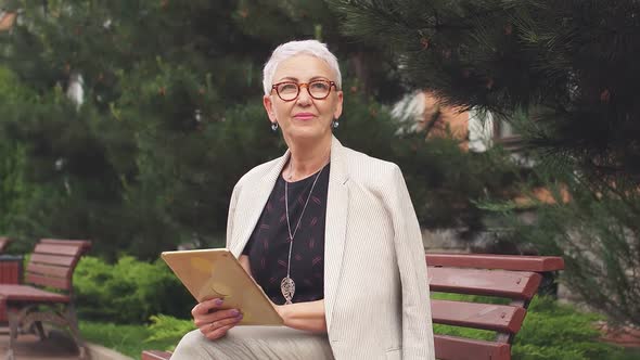 Business Woman in White Jacket Relaxes in Park Using Tablet