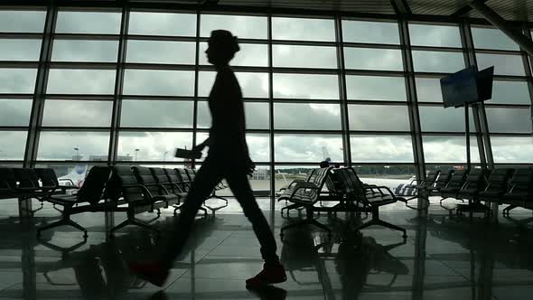 Travelers Walking Along Window in Airport Terminal, People Silhouettes Walking.