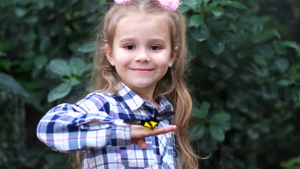 The Little Princess Holds a Butterfly on Her Hand Looks at the Frame and Smiles