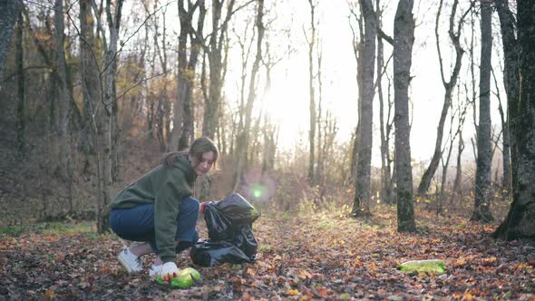 A Beautiful Girl Goes Against the Background of Trees and Sunlight and Cleans Nature of Plastic