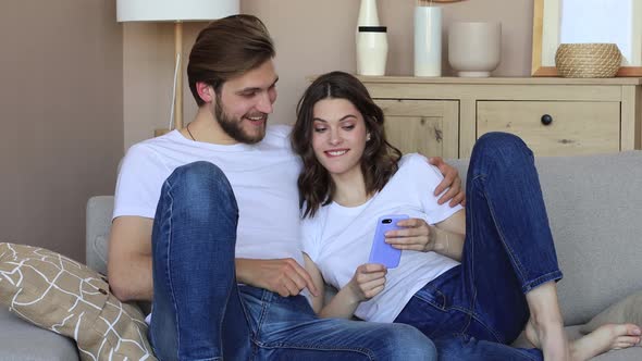 Happy couple sitting and planning new home decoration at home with a smartphone