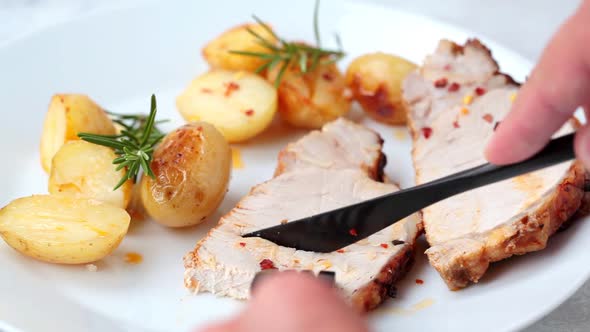 Cut a piece of baked pork loin with potatoes on white plate.