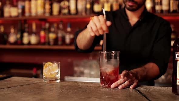 Bartender pouring mixed liqueur into prepared glass through cocktail strainer