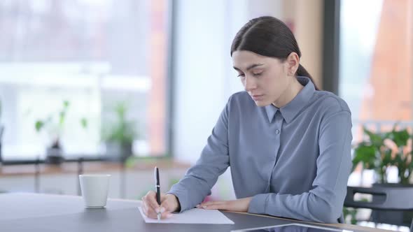 Young Latin Woman Writing on Paper in Office