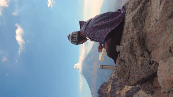 Man sitting outside on rocks  holding a book and looking the landscape