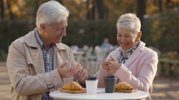 Senior Couple Disinfecting Hands with Sprayer Enjoying Snack At Outdoor Cafe