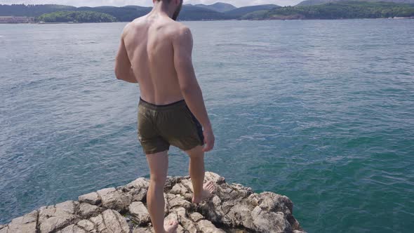 Man Jumps Into Water From The Rock Slope. Summer Fun Lifestyle.