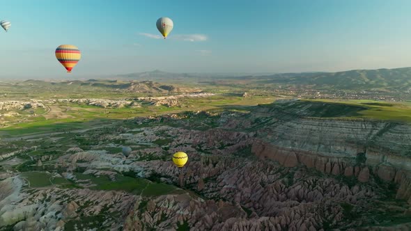 Hot air balloons fly over the mountainous landscape of Cappadocia, Turkey.