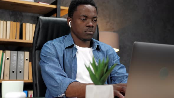 African American Man in Wireless Earphones Works for Laptop Typing on Keyboard