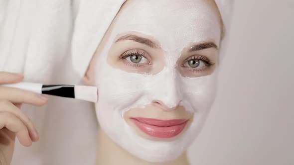 Smiling Young Woman with a Mask on Her Face and a Towel on Her Head at Home on White Background