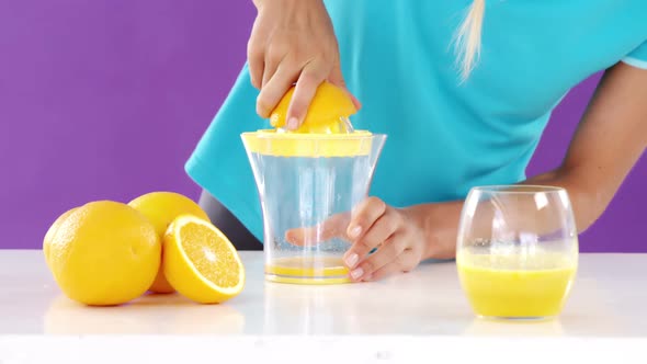 Woman preparing sweet lime juice from juicer against violet background