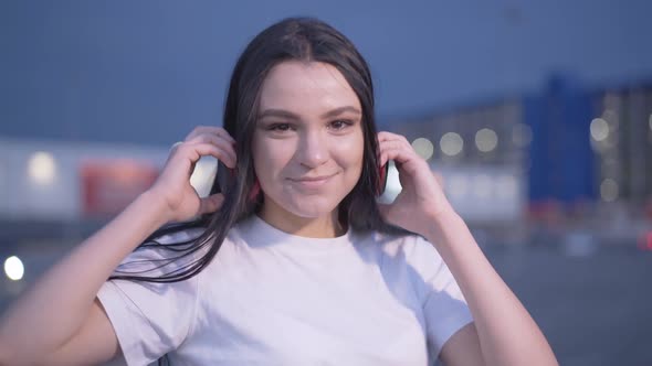 Charming Positive Young Woman Turning To Camera on Empty Parking Lot and Taking Off Headphones