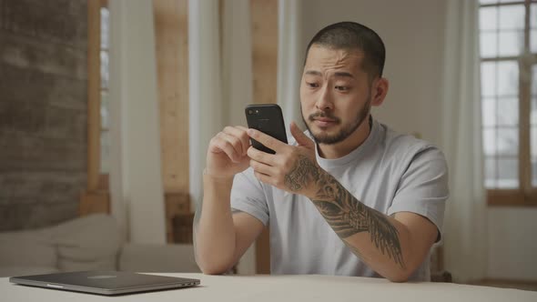 A Tattoed 20s Asian Man with Like and Dislike Facial Expressions While Browsing on Smart Phone