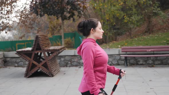 Nordic Walking concept. Young focused chubby female walking up the stairs with nordic poles