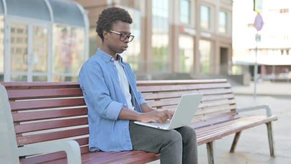 Coughing Young African Man Using Laptop While Sitting Outdoor on Bench