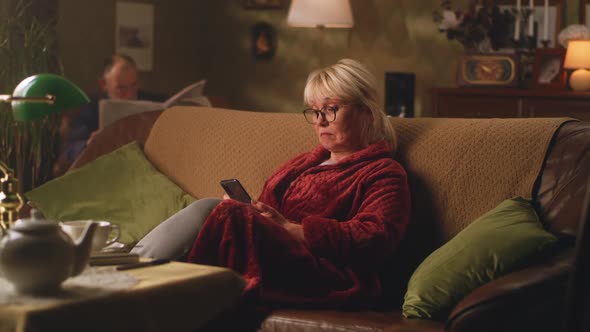 Sad Senior Female with Smartphone Resting on Couch