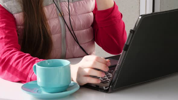 Teenager Girl in Headphones, Working on Laptop, Chatting Online, on Open Balcony. Spring Sunny Day