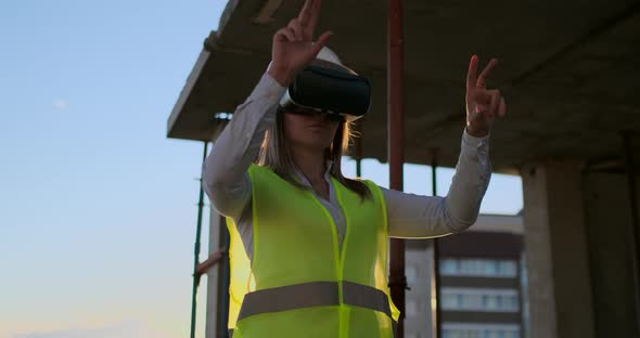 Woman Expert Engineer Builder in VR Glasses and Helmet Checks the Progress of Skyscraper