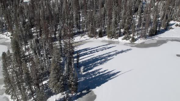 Flying backwards above forest and lake frozen in winter