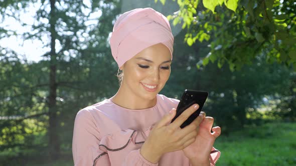 Beautiful Muslim Woman in Turban with Phone on Background of Trees