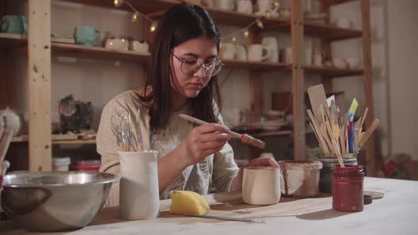 Young Woman Potter Working in Art Studio  Finishing the Final Ceramic Product By the Table