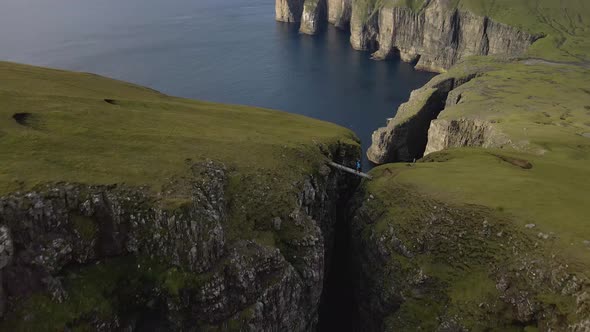 Drone Over Hiker Crossing Bridge Between Cliffs