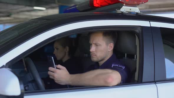 Man and Woman Cop Using Smartphones Sitting in Patrol Car, Monitoring City App