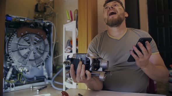 A Man Fixes a Washing Machine and Watches Instructions on His Phone