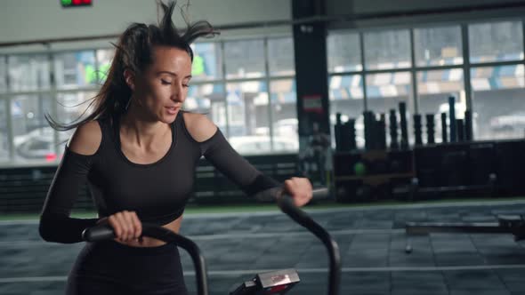 Young female athlete trains cardio on a bicycle with a fan, cardio and endurance training