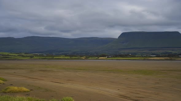 Time Lapse of sand sea coast of Ireland with hills in the distance and moving clouds in the sky.