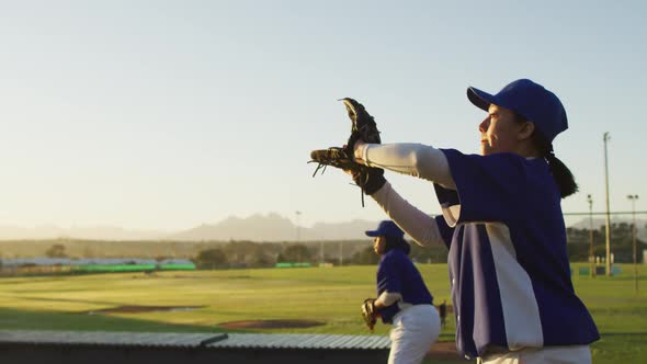 Diverse group of female baseball players practicing on pitch, throwing and catching ball