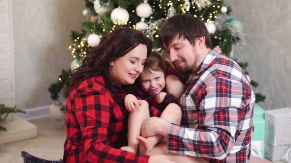 Dad Mom and Little Daughter in Red Plaid Pajamas Playing at the Christmas Tree