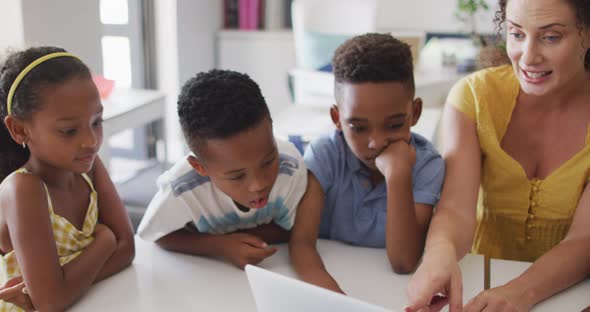 Video of happy caucasian female teacher and african american pupils using laptop