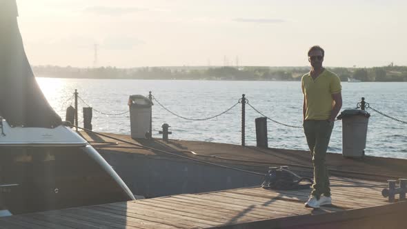 Handsome Successful Man Walking To His Yacht. A Man Goes Along the Pier Near Sailing Boat at Sunset.