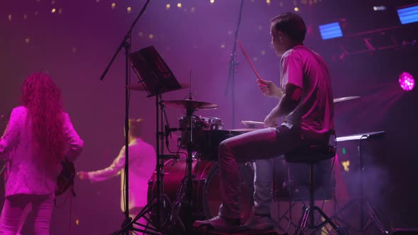 Musician Drummer Playing Musical Instrument Against Backdrop of Bright Neon Lights