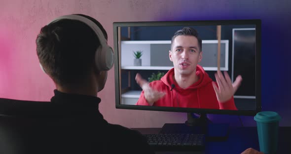 Rear View of a Young Man with Headphones Watching a Video Blog Indoors