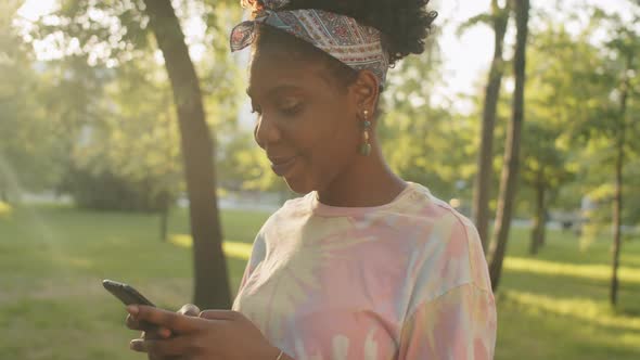 Cheerful Afro-American Woman Using Smartphone Outdoors