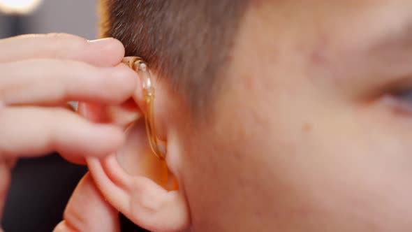 A Young Man Removes a Digital Hearing Aid with an Individual Earpiece From His Ear. Deafness. Close