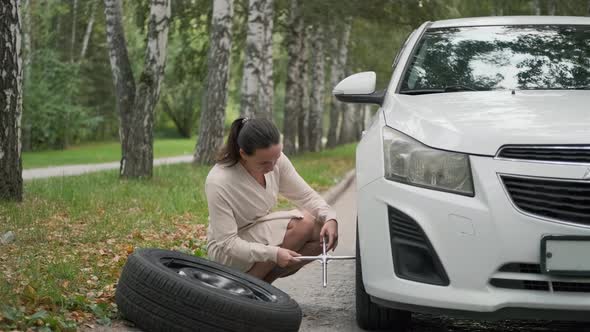 Young Woman Trying to Change a Wheel on a Road