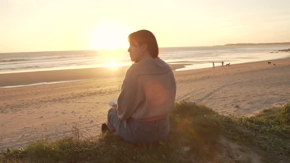 Traveling woman sitting on hill against sunset sky near sea