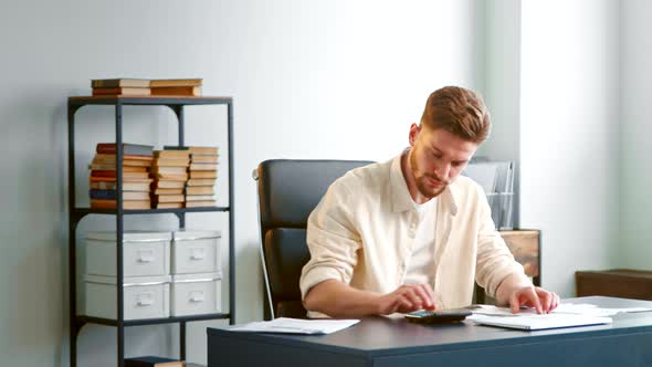 Professional entrepreneur in yellow shirt counts receipts summing up on calculator