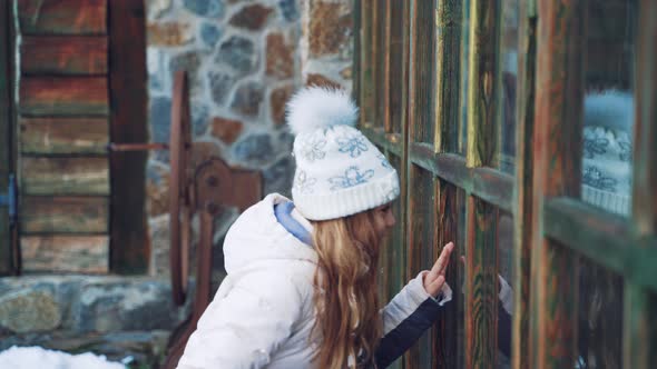 Little Girl with Long Hair and in Warm Clothes is Peeping Through the Window 