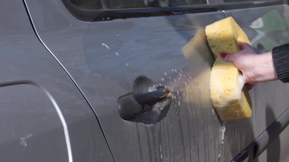 Car wash. A woman washes the body of a car with a sponge