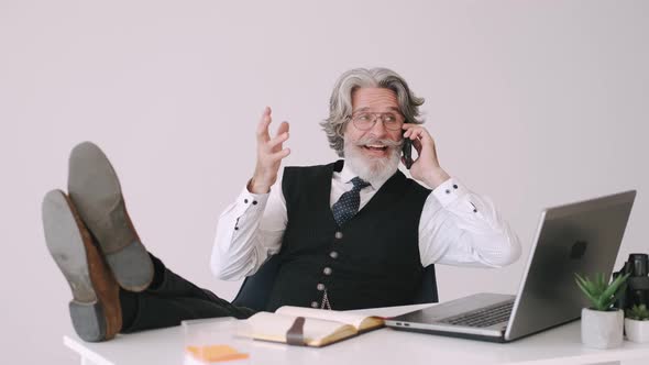 Stylish Old Businessman Talking By Phone in Office