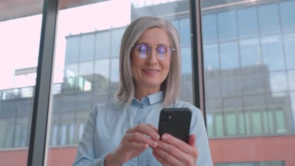 Middle Age 60s Old Senior Businesswoman is Using a Smartphone in an Office