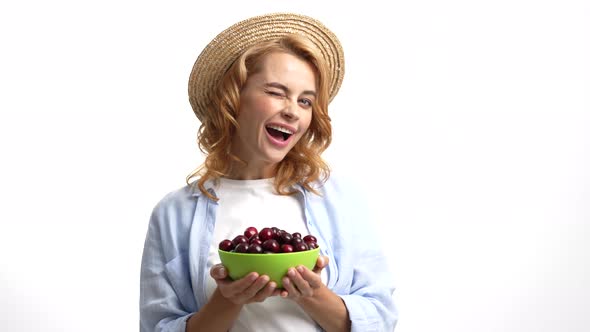 Cheerful Girl Farmer Winking in Straw Summer Hat Sharing Cherry Bowl Selective Focus Organic Food