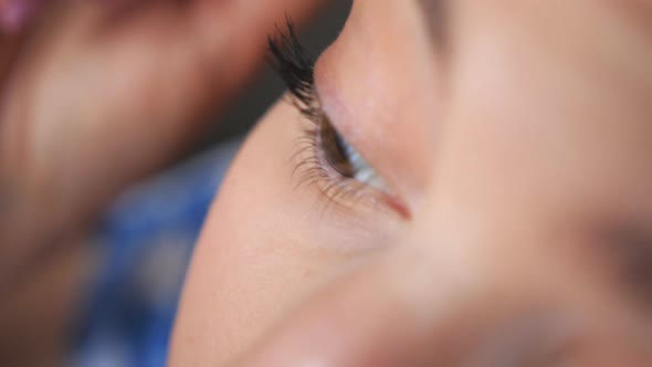 Close Up Face of Young Woman Applying Cosmetic on Eyelashes. Pretty Girl with Wide Opening Eyes