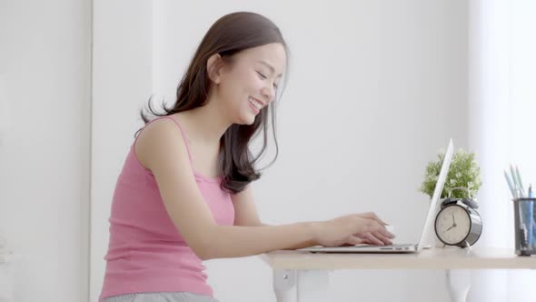 Beautiful young freelance asian woman smiling working and typing on laptop computer at desk office.